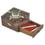 Woodino Drawer Ashtray made of Sheesham wood features a metal insert, decorative inlays with an elephant motif, and a red felt-lined drawer that holds two cigarettes and a matchstick. The word Woodino appears across the image.